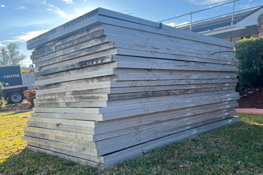 Large stacks of silver-framed solar panels sit on a green lawn.