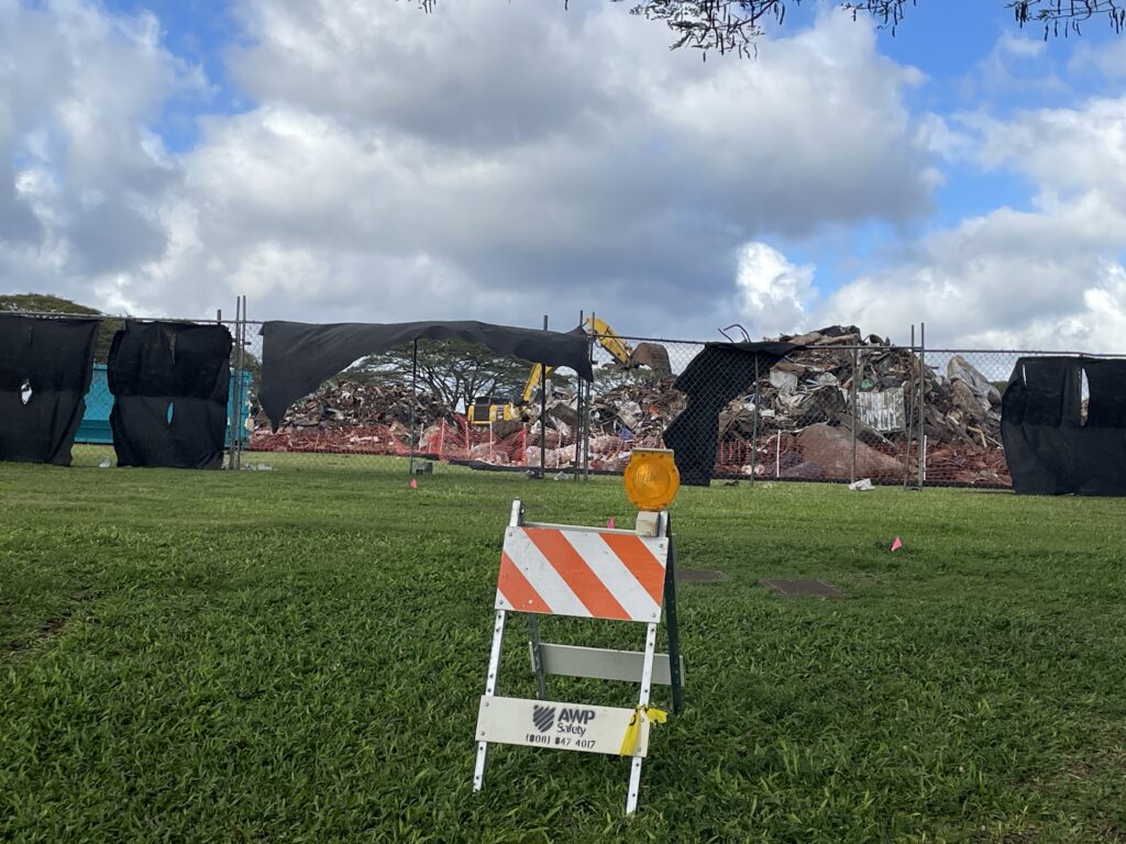 A black screen hangs on a fence surrounding debris from massive flooding from a storm that hit Oahu in March 20206.