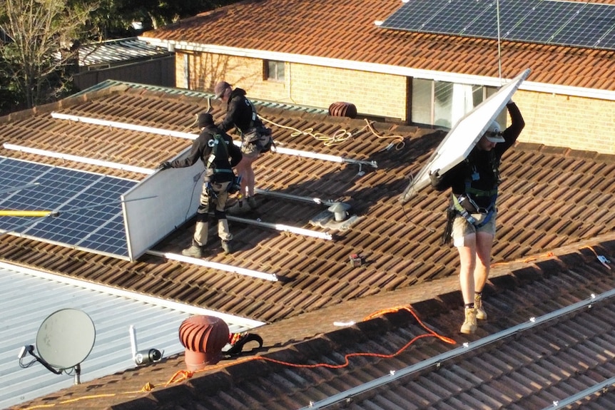 Men in black clothes stand on a terracotta tile roof and remove solar panels.